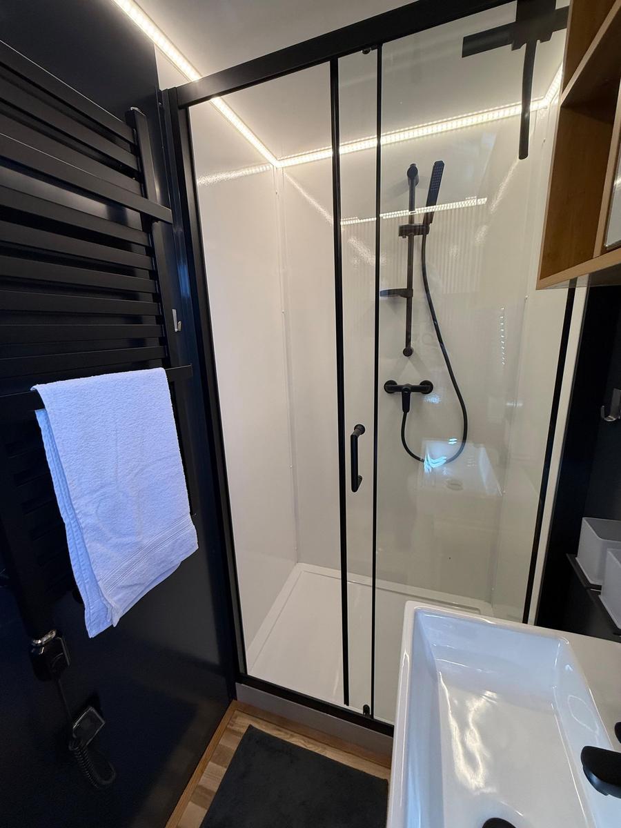 Shower with glass enclosure, handheld shower, and towel warmer.