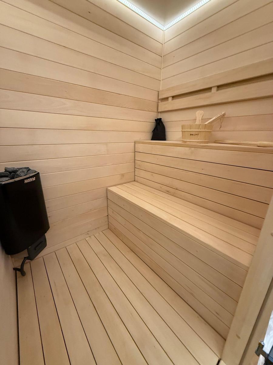 Sauna with wooden bench, basket, and heater on the wall.