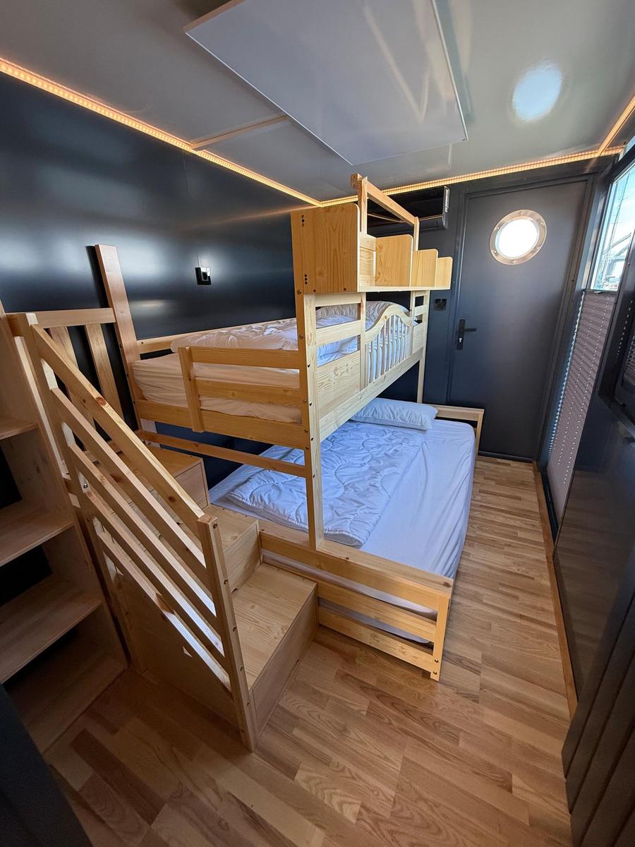 Room with bunk bed and wooden staircase. Wooden floor and dark walls.