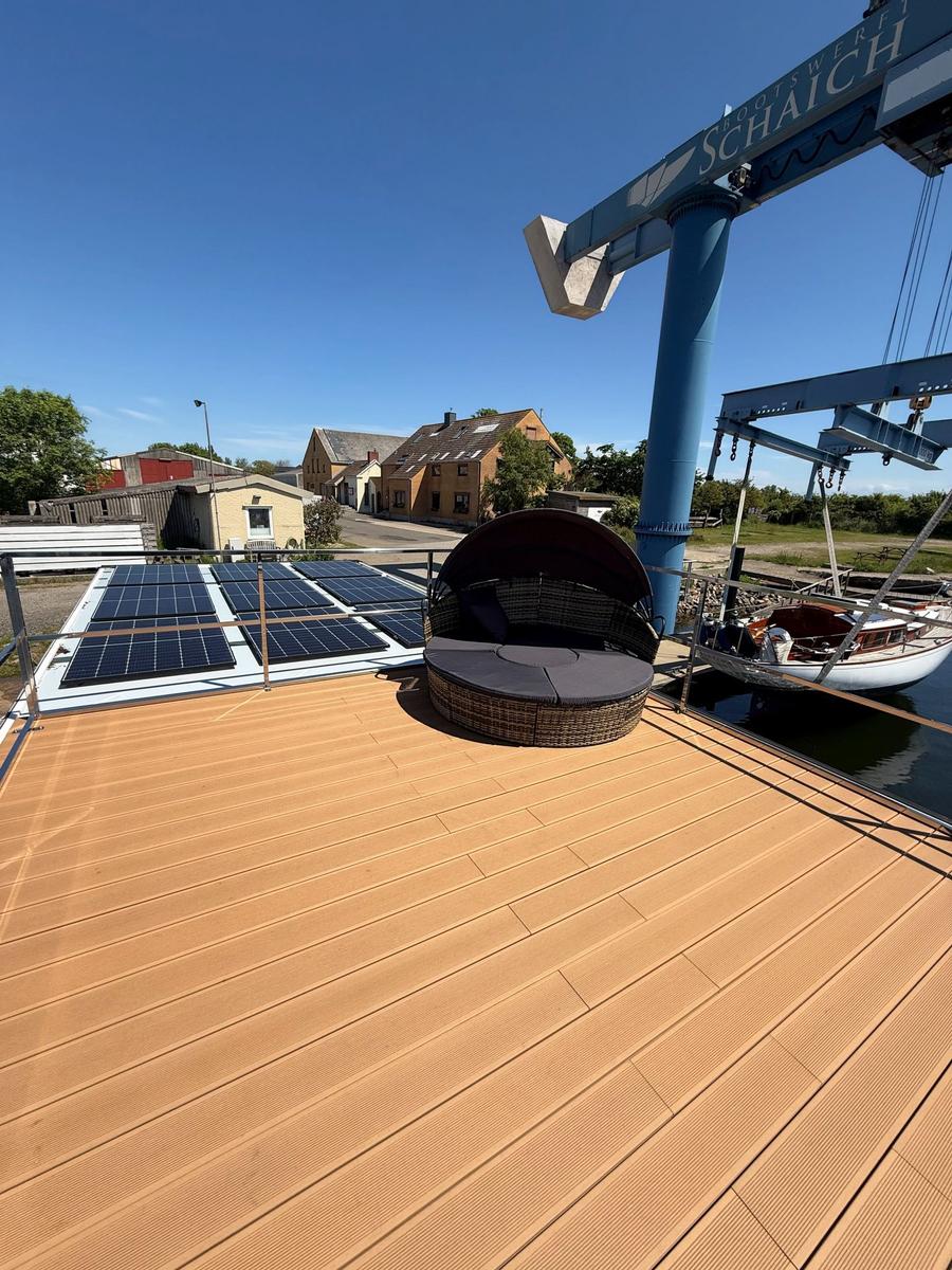 Deck with sun lounger, solar panels, and view of harbor and cranes.