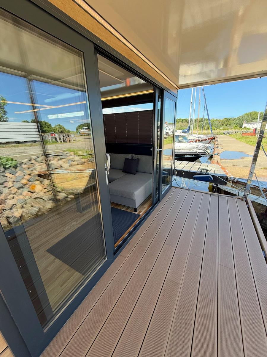 Deck with wooden planks and view of marina. Glass doors lead to interior space.