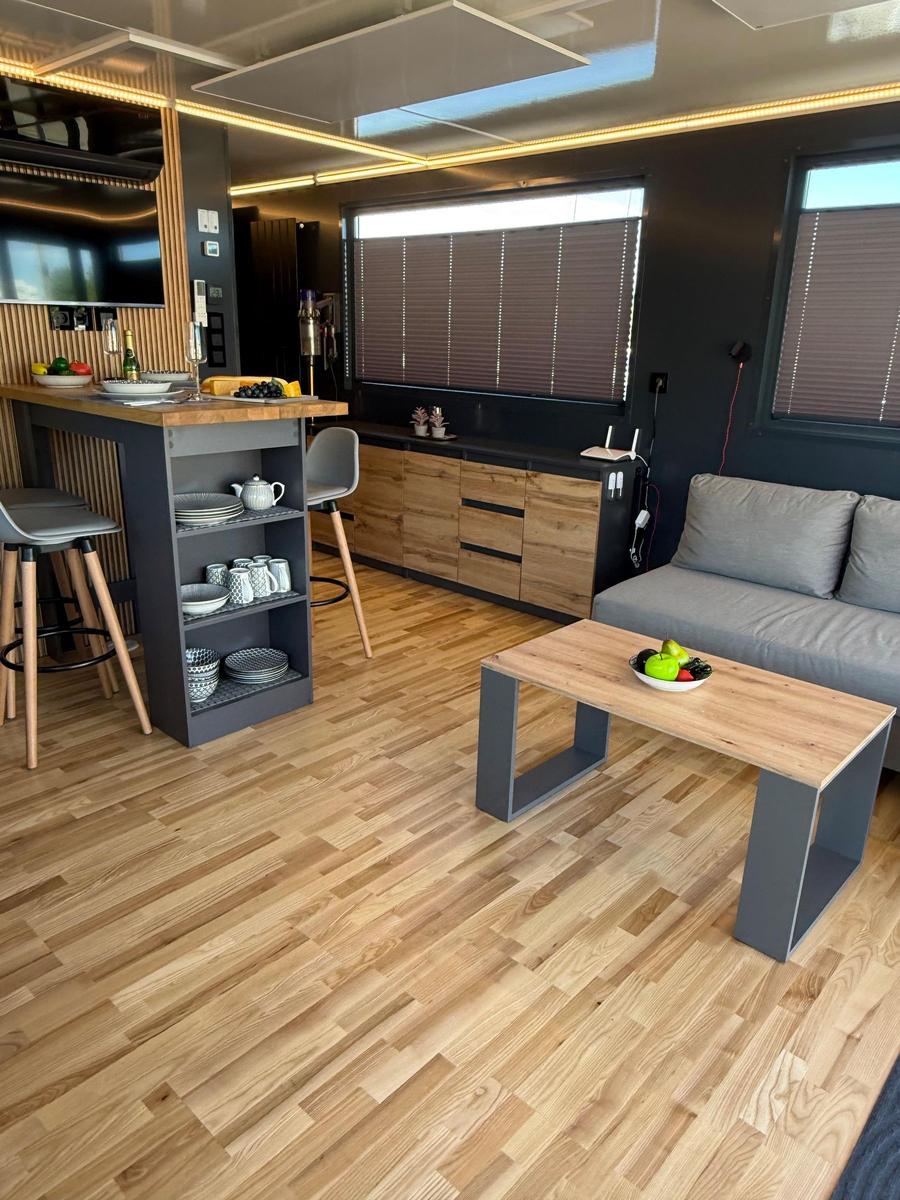 Living kitchen with wooden floor, sofa, dining table, and kitchen island with stools.