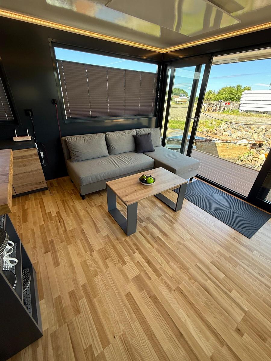Living area with sofa, table, and wooden floor. Entrance to terrace with garden view.