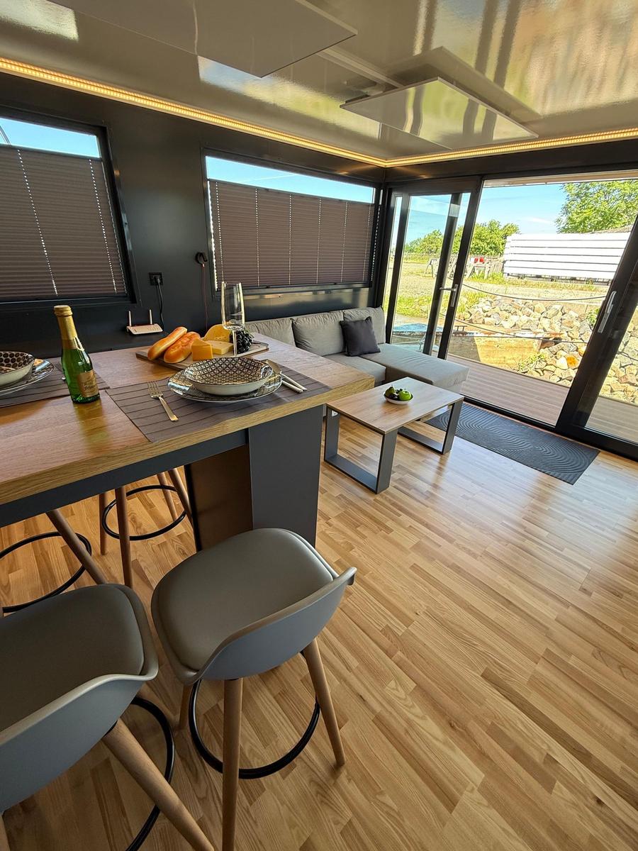 Dining area with wooden floor and seating. Passage to terrace with garden view.