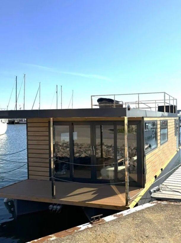 Modern houseboat with wooden cladding and large glass area by the water.