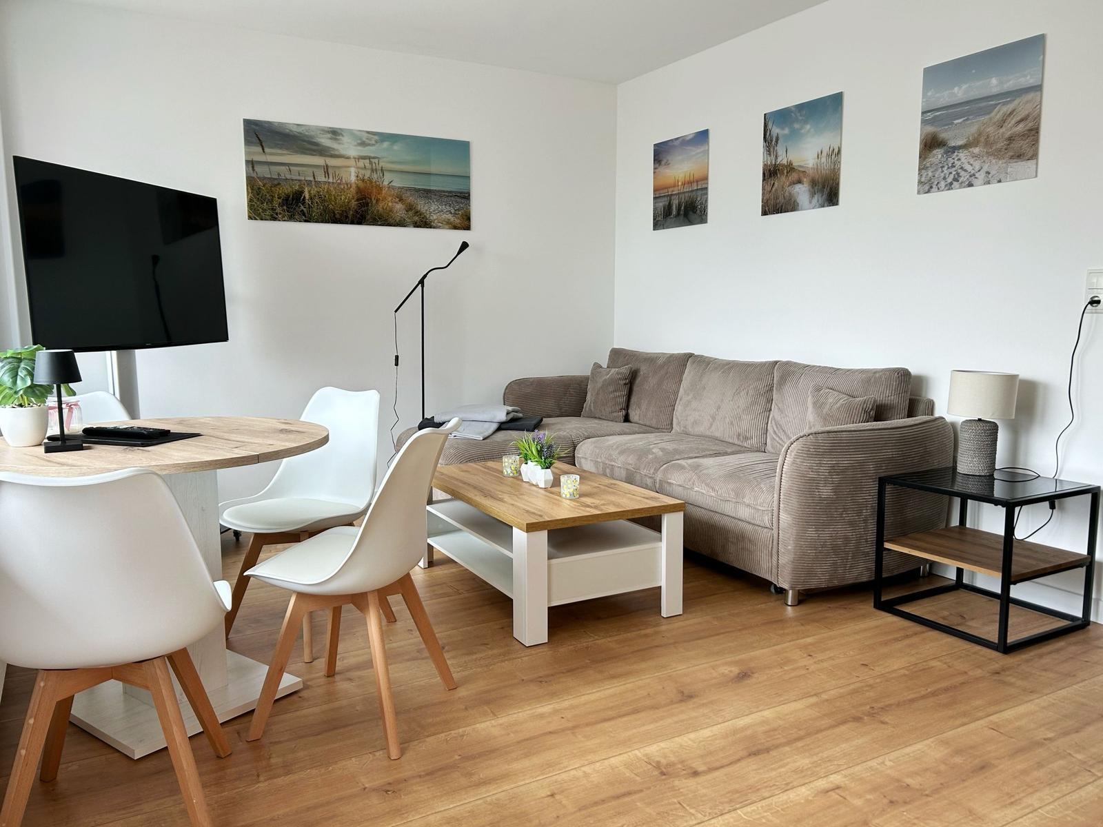 Wohnzimmer mit Sofa, Esstisch und Wandbildern