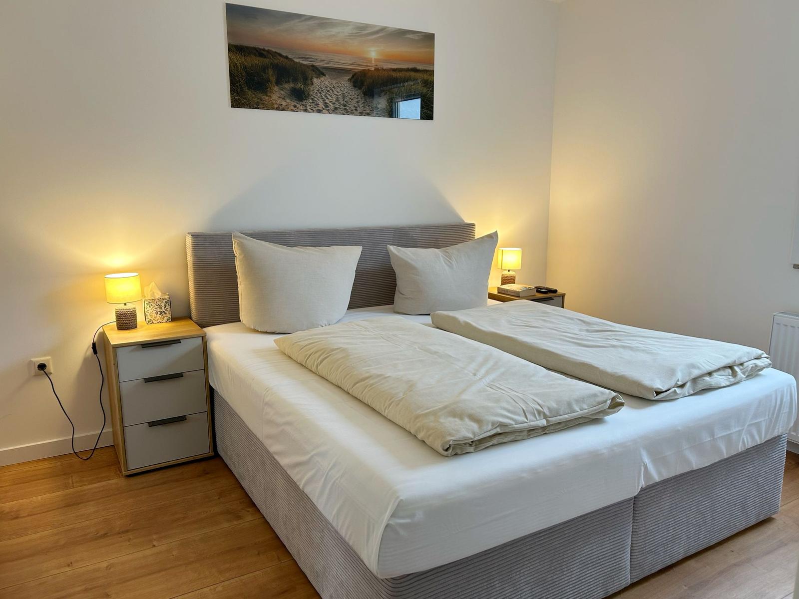 Schlafzimmer mit Doppelbett, Nachttischen und Wandbild.