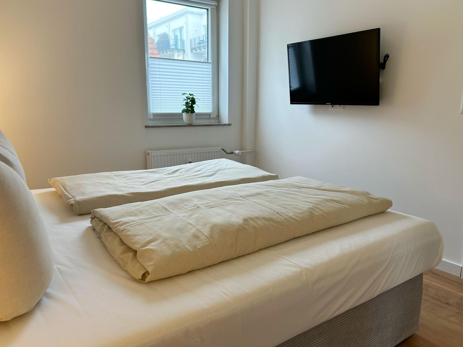 Schlafzimmer mit Bett, Fenster und Wandfernseher.