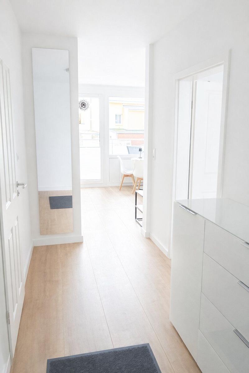 Flur mit Holzboden, Spiegel und Schrank. Durchgang zu Wohn- und Essbereich.