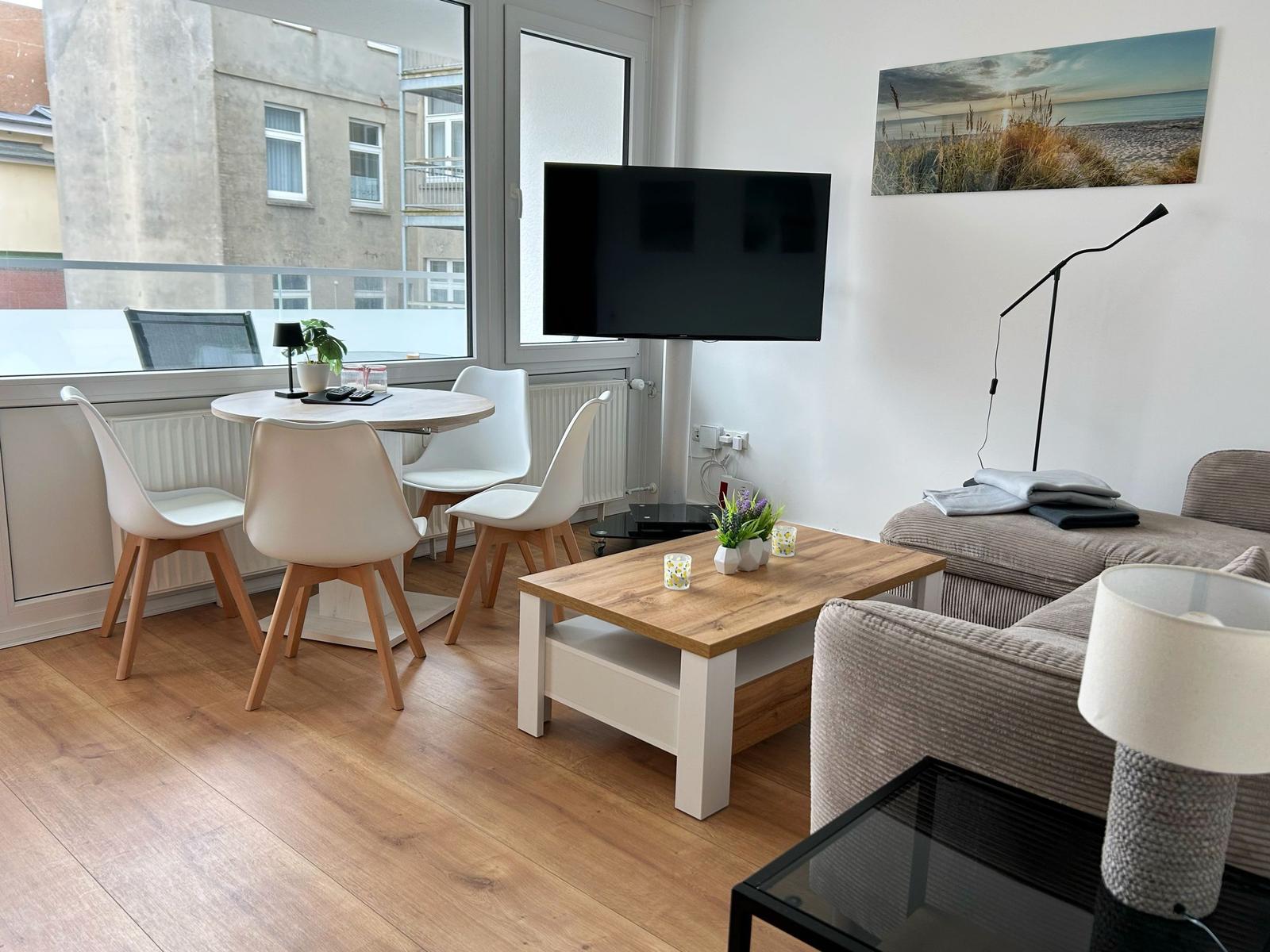 Wohnzimmer mit Esstisch, Sofa und Fernseher. Holzboden und großes Fenster.