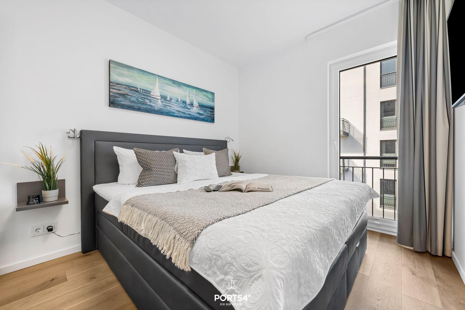 Schlafzimmer mit Bett, Wandbild und Balkonansicht.