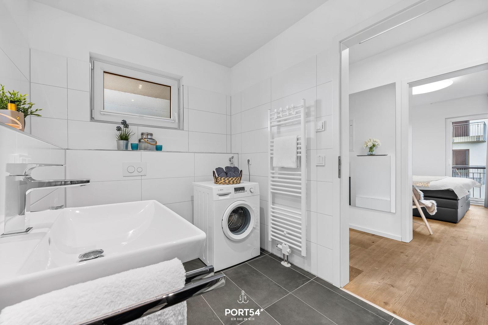 Badezimmer mit Waschmaschine, Handtuchhalter und Blick in Schlafzimmer.