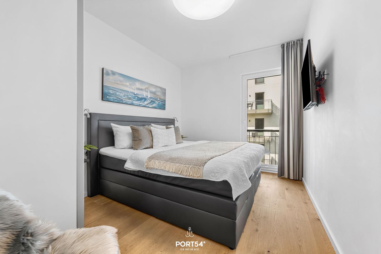 Schlafzimmer mit Bett, Wandbild und Balkontür.