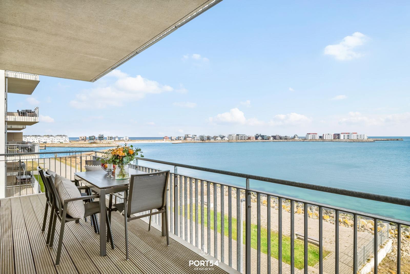 Terrasse mit Tisch und Stühlen bietet Meerblick. Hintergrund: Wasser und Gebäude.
