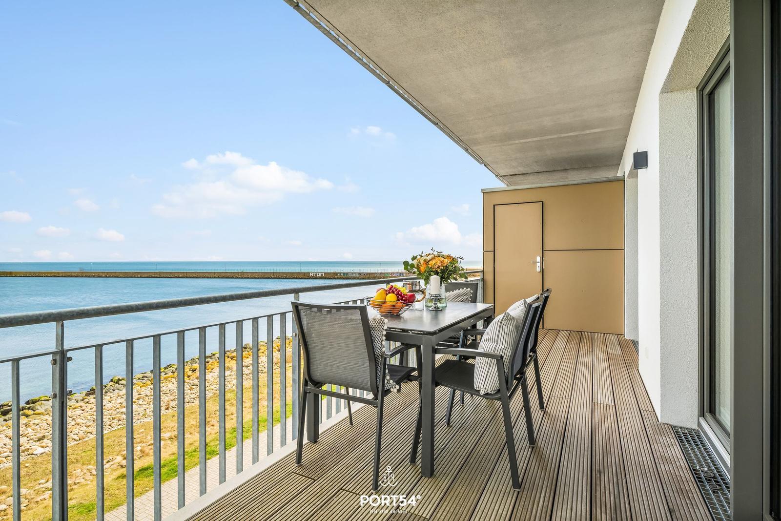 Terrasse mit Tisch und Stühlen, Blick auf Meer und Hafen.