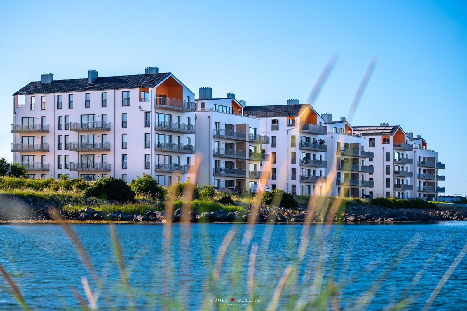 Moderne Wohnhäuser am Wasser mit Balkonen und grüner Umgebung.