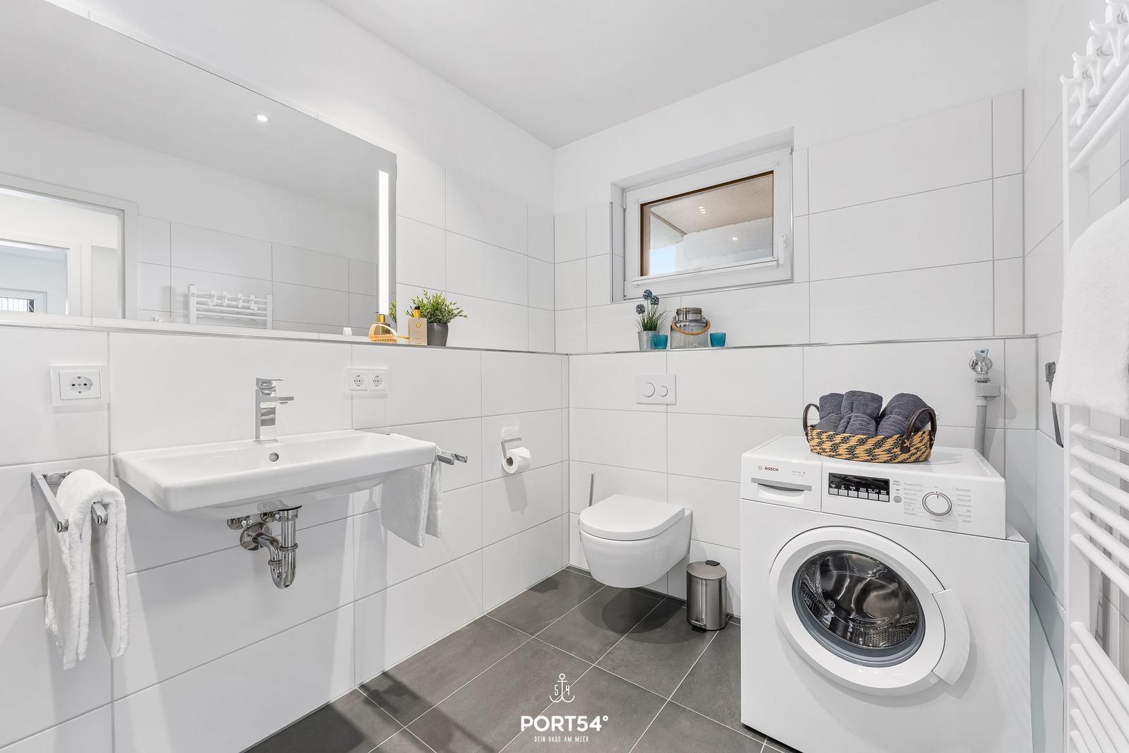 Badezimmer mit Waschmaschine, Spiegel und Toilette.