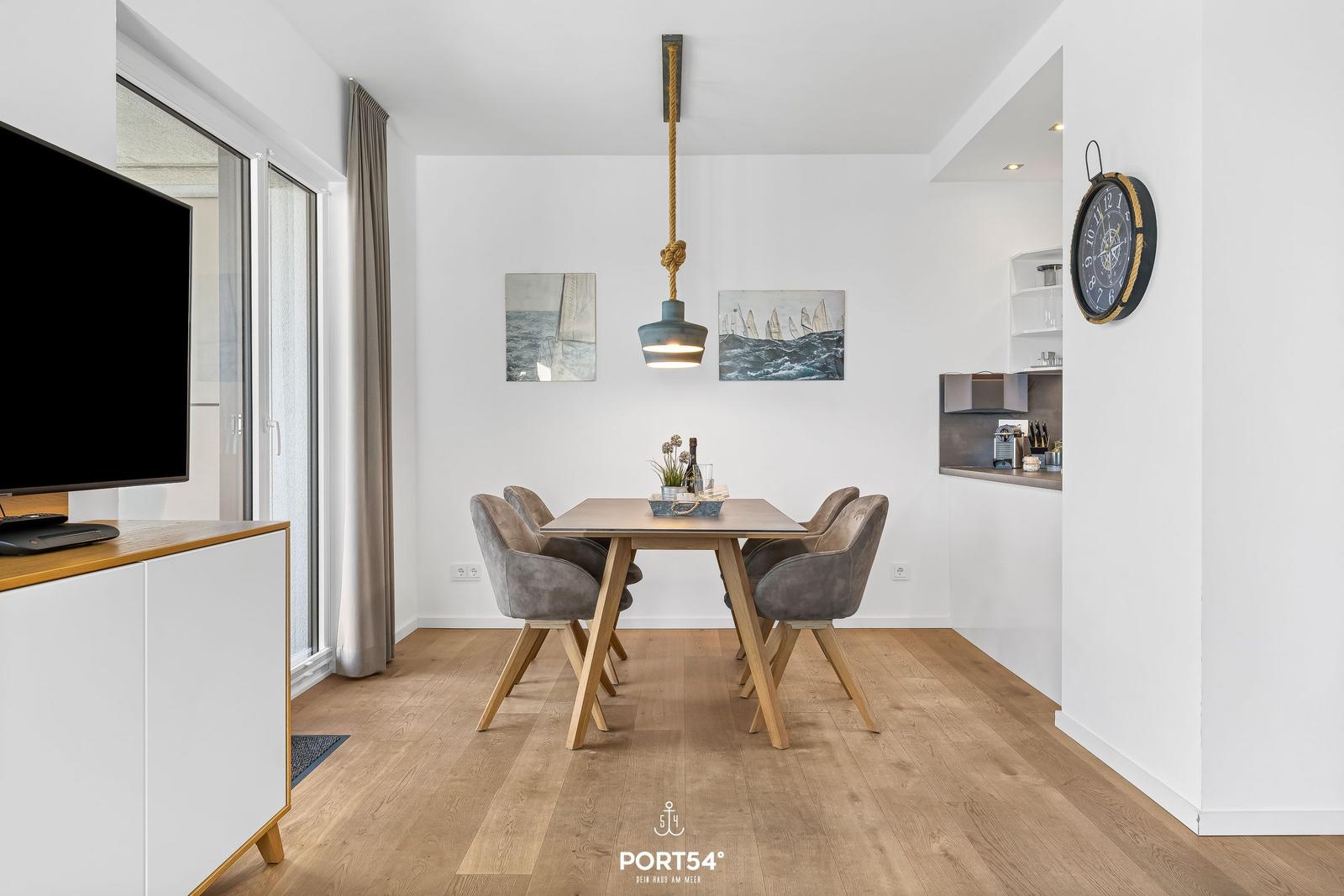 Essbereich mit Tisch, Stühlen und Wandbildern. Holzfußboden und hängende Lampe.