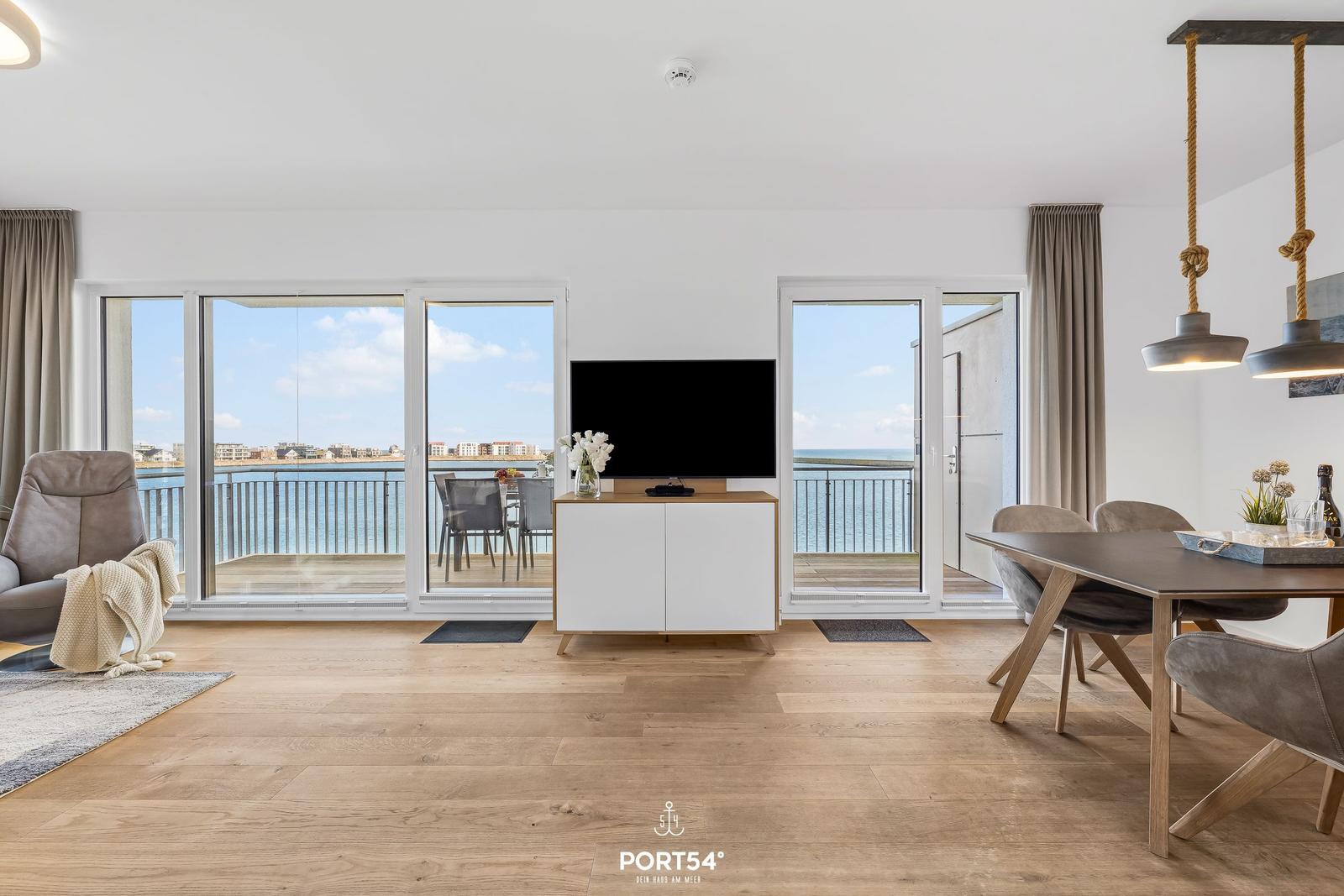 Wohn- und Essbereich mit Meerblick und Balkon. Holzboden und moderne Einrichtung.