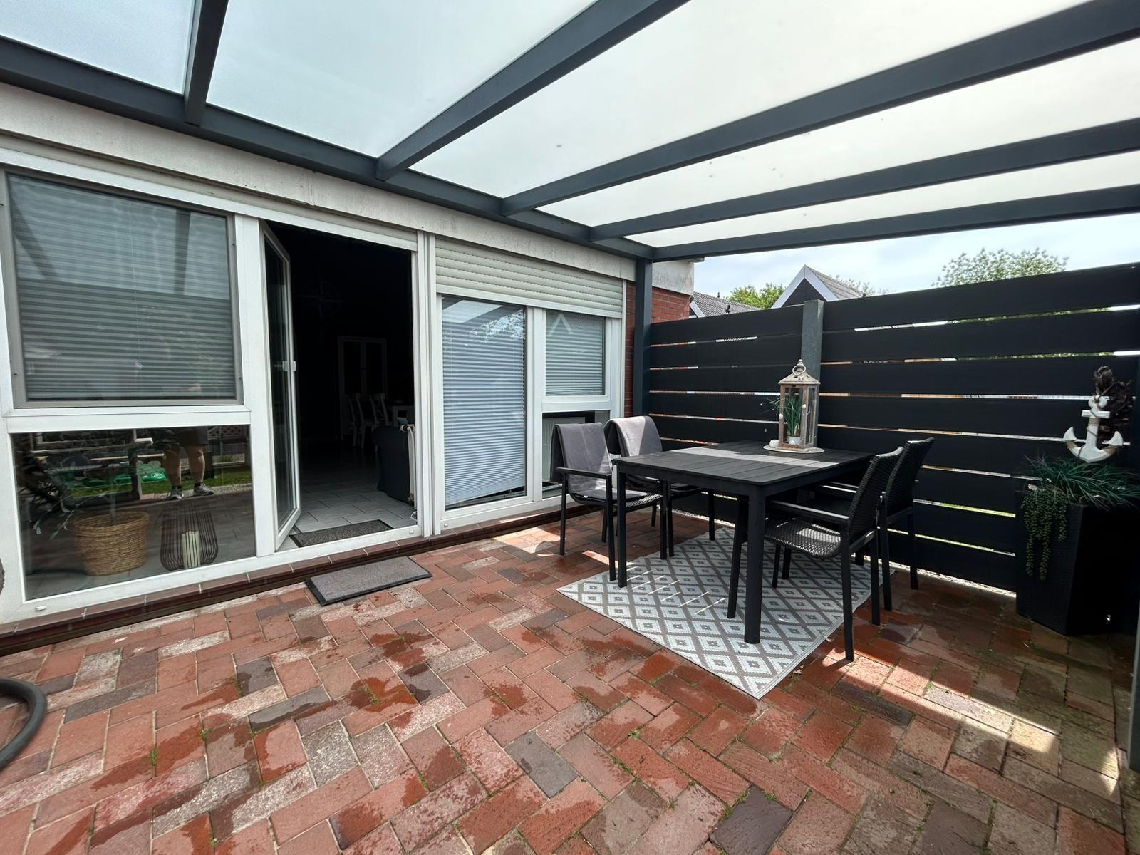 Terrace with seating under glass roof. Red brick paving and black wooden fence.