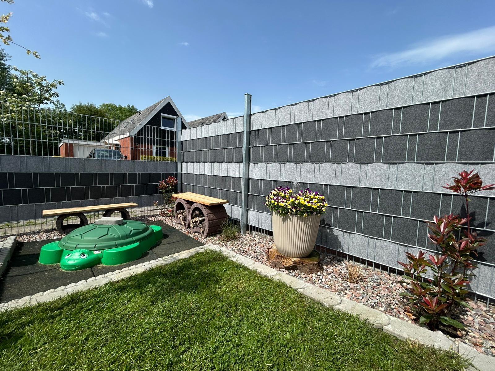 Backyard with playground, flower pot, and stone wall. Lawn and gravel area.