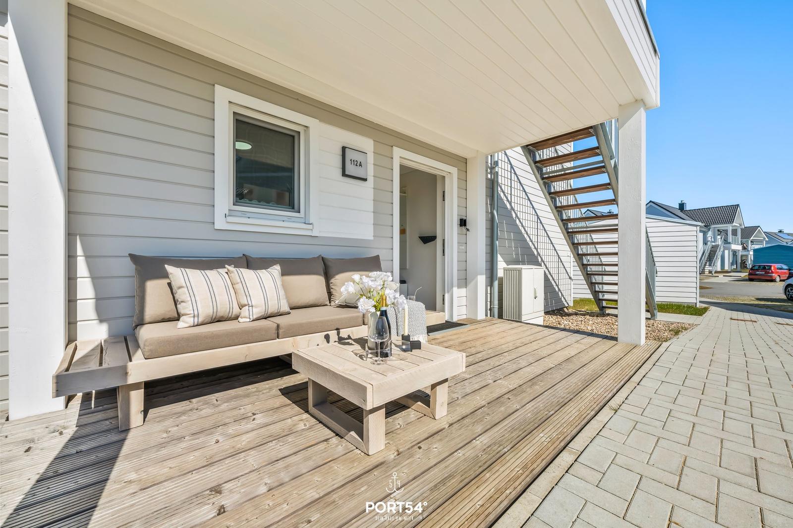 Terrasse mit Sofa, Tisch und Blumen. Hintergrund: Haus mit Treppenhaus.