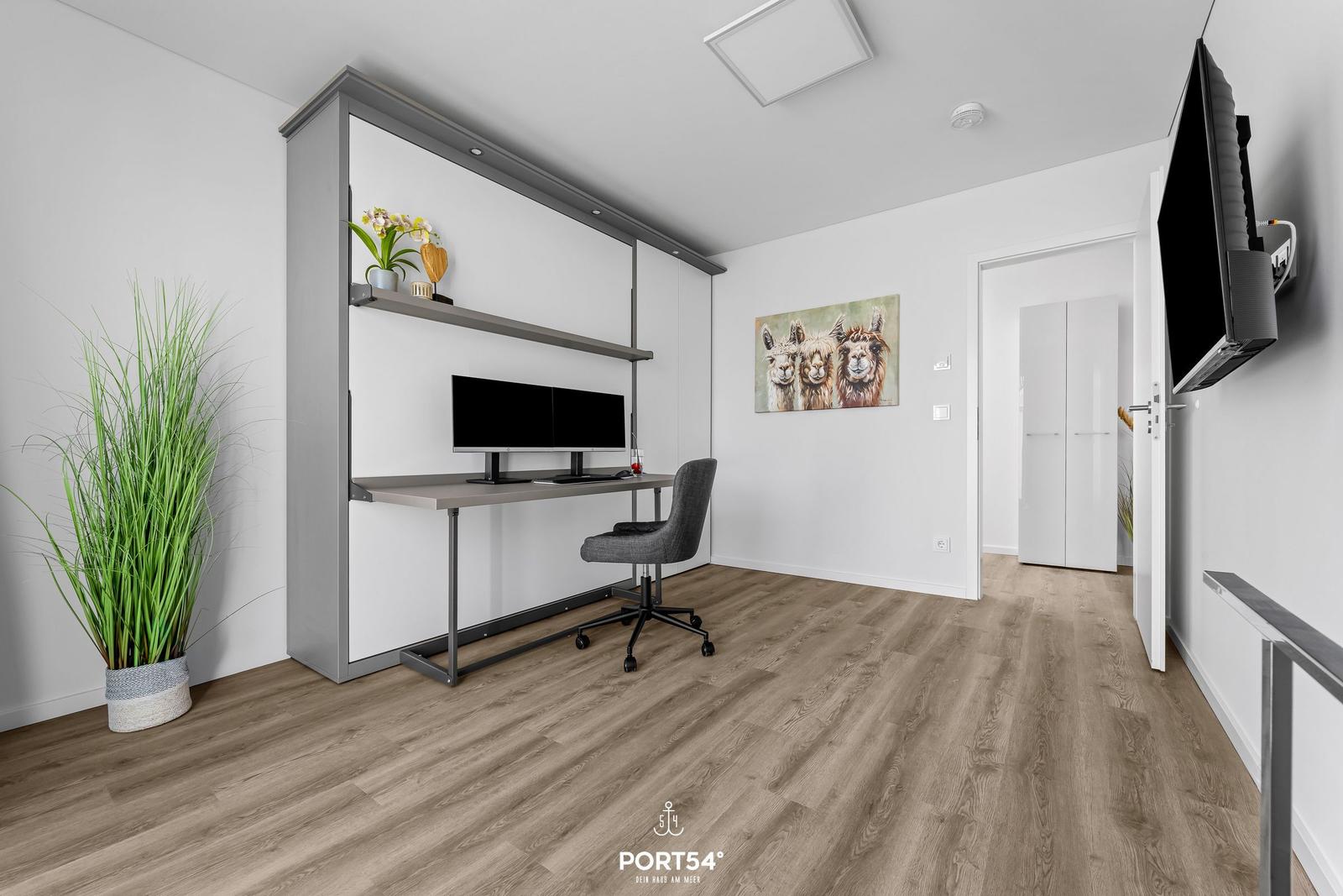 Arbeitszimmer mit Schreibtisch, Monitor, Stuhl und Wandbild von Lamas.