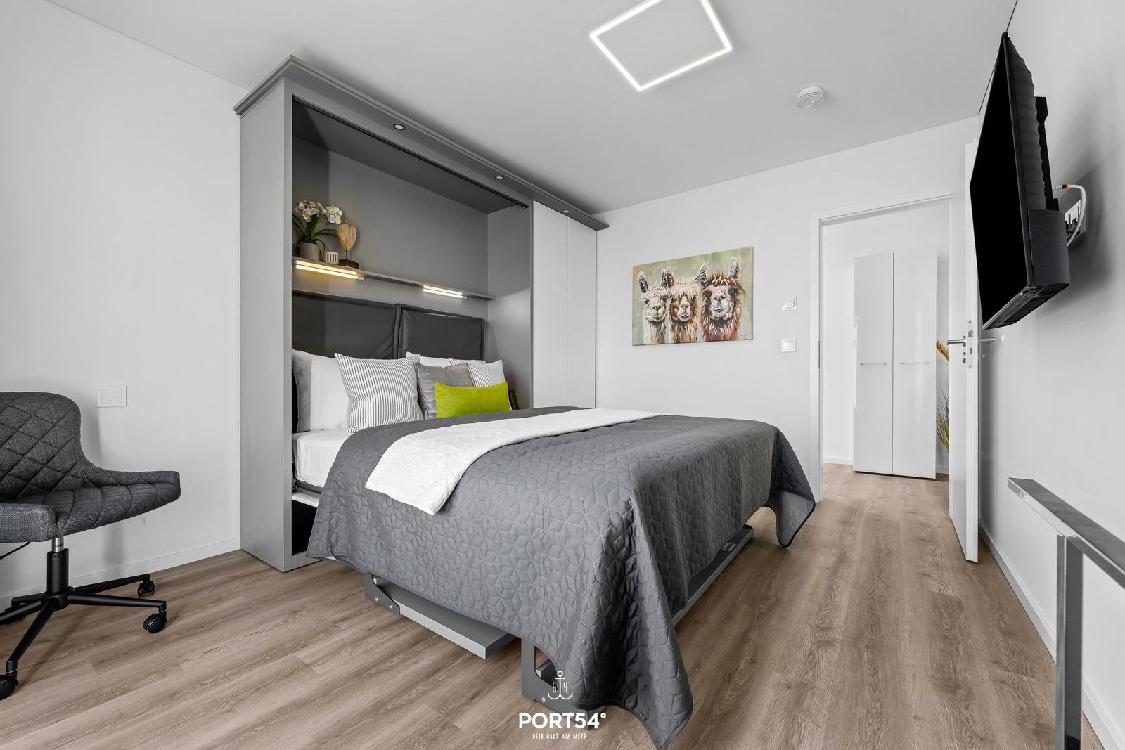 Schlafzimmer mit Bett, Schreibtischstuhl und Wandbild von Lamas.