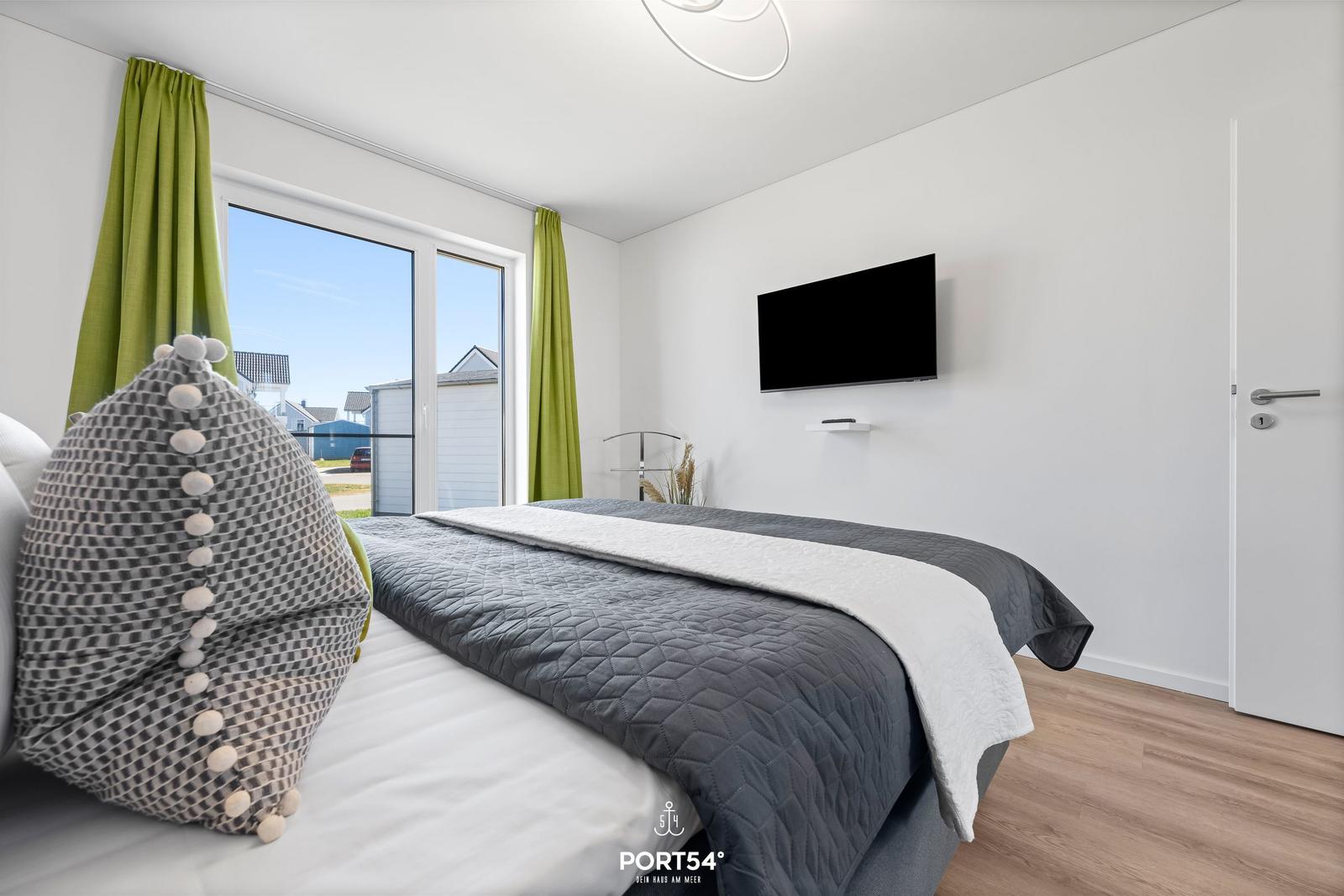 Schlafzimmer mit Bett, Fenster, TV und grünen Vorhängen.