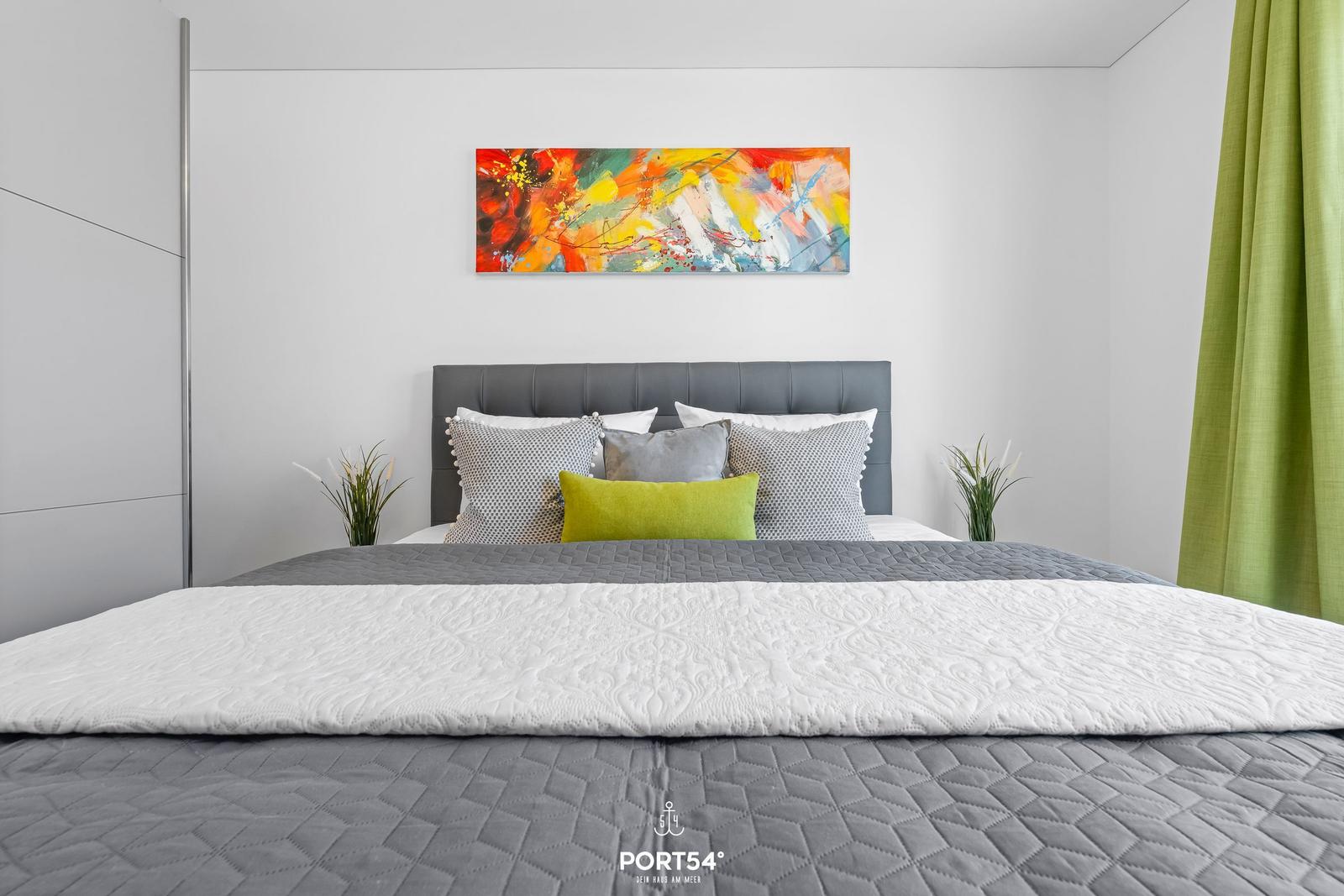 Schlafzimmer mit Bett, Wandbild und grünen Vorhängen.