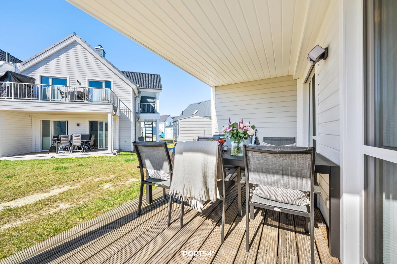 Terrasse mit Tisch, Stühlen und Blumen. Hintergrund: Garten und Nachbarhaus.