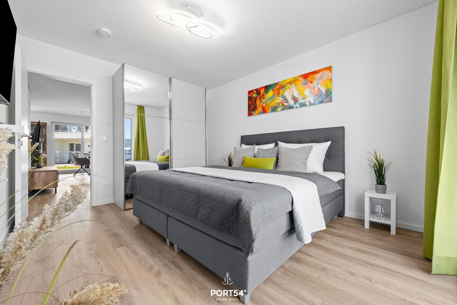 Schlafzimmer mit Doppelbett, Wandbild und Holzboden. Blick in Wohnbereich.