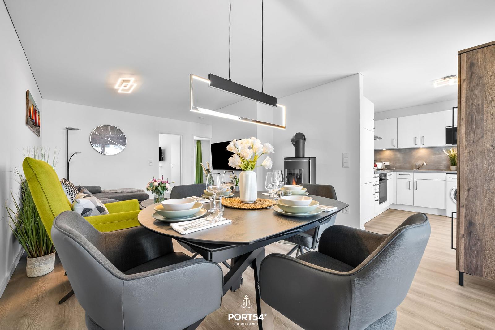 Essbereich mit Tisch und Stühlen, Küche im Hintergrund, Holzboden und moderne Beleuchtung.