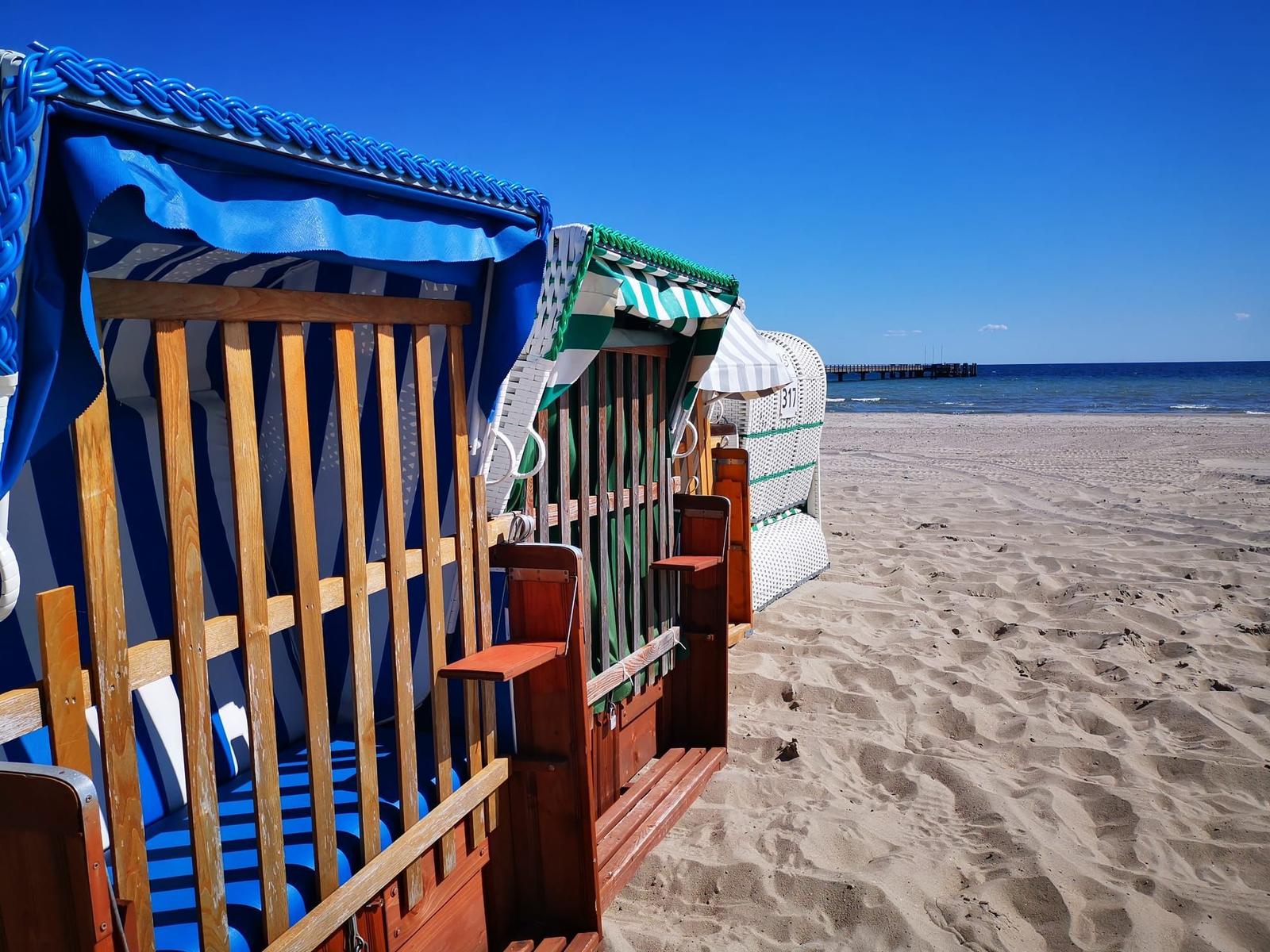Strandkörbe mit blau-weißem und grün-weißem Muster stehen am sandigen Strand.