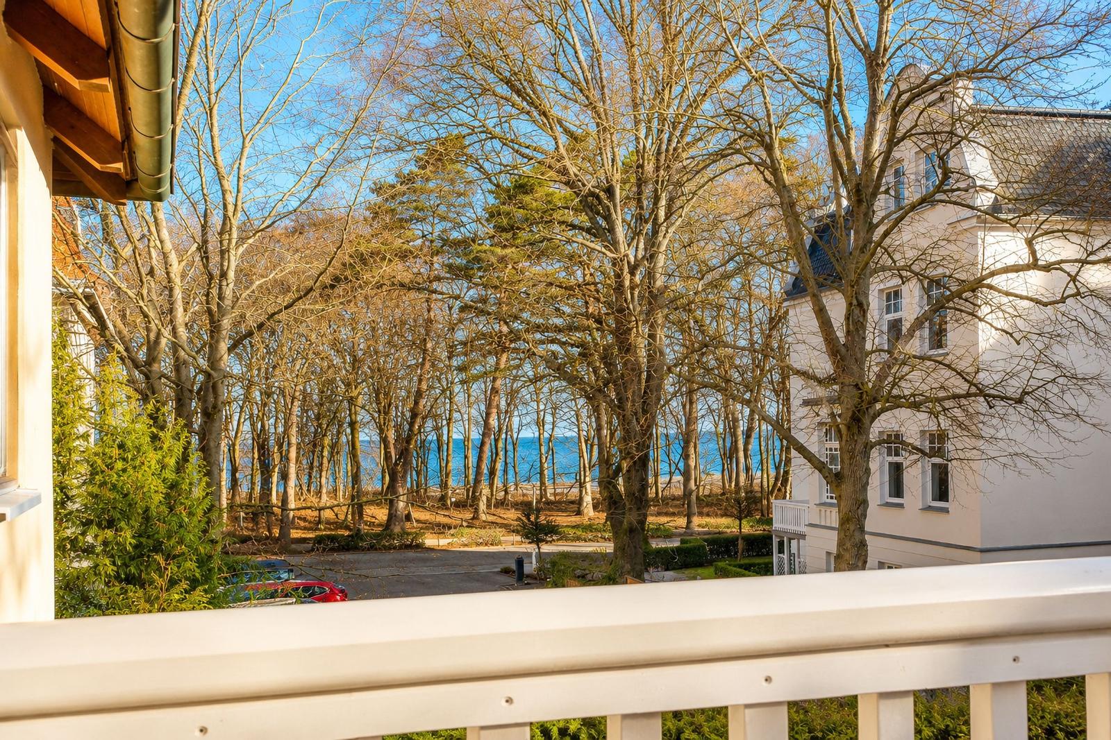 Blick vom Balkon auf Wald und Meer mit weißem Haus im Hintergrund.