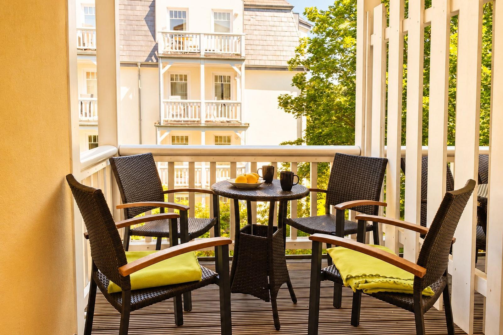 Terrasse mit Tisch und vier Stühlen, grüne Kissen, Blick auf Gebäude und Bäume.