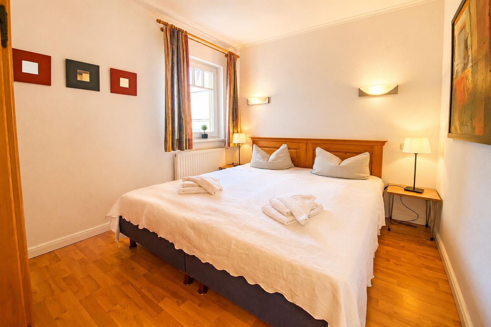 Ein Schlafzimmer mit Doppelbett, Holzboden und Fenster mit Vorhängen.