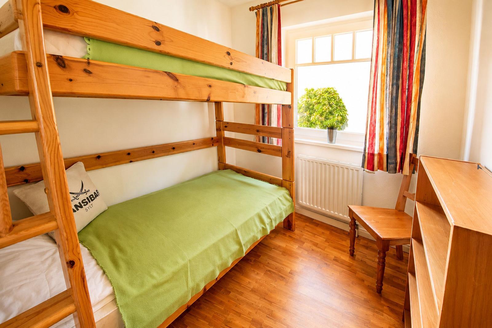 Ein Schlafzimmer mit Doppelstockbett, Holzboden und Fenster mit Vorhängen.