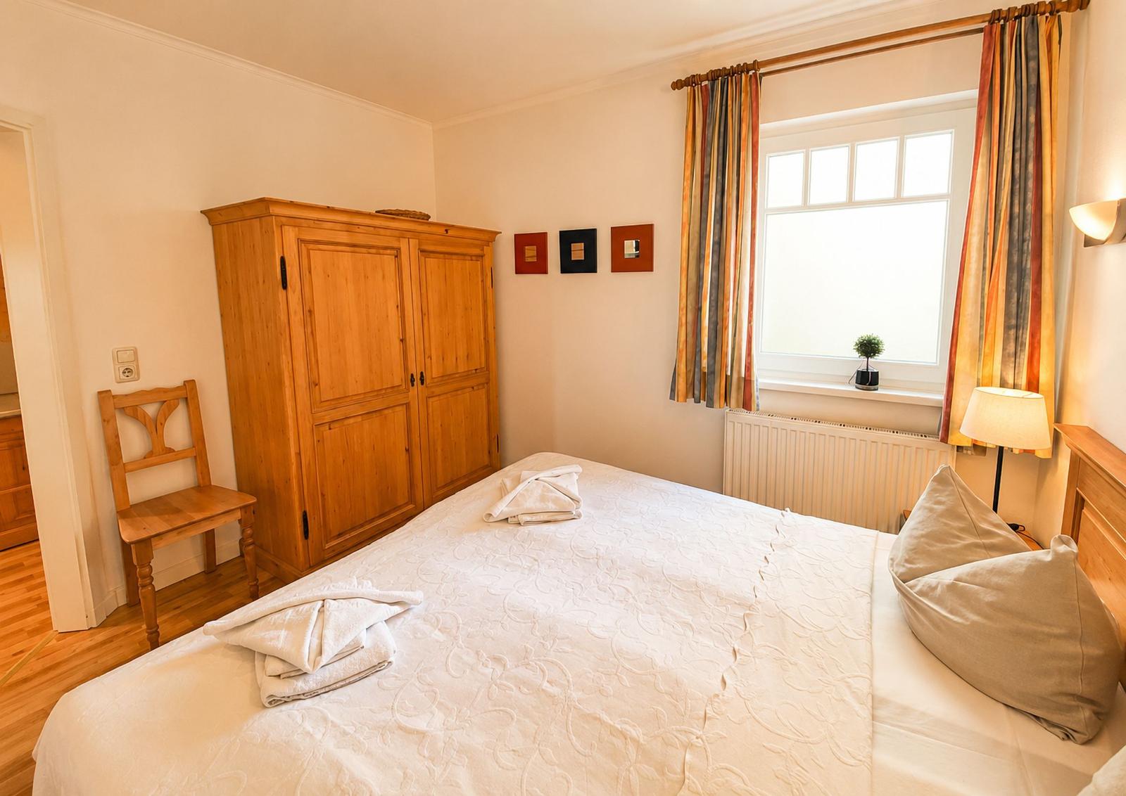 Schlafzimmer mit Bett, Holzschrank und Fenster mit Vorhängen.