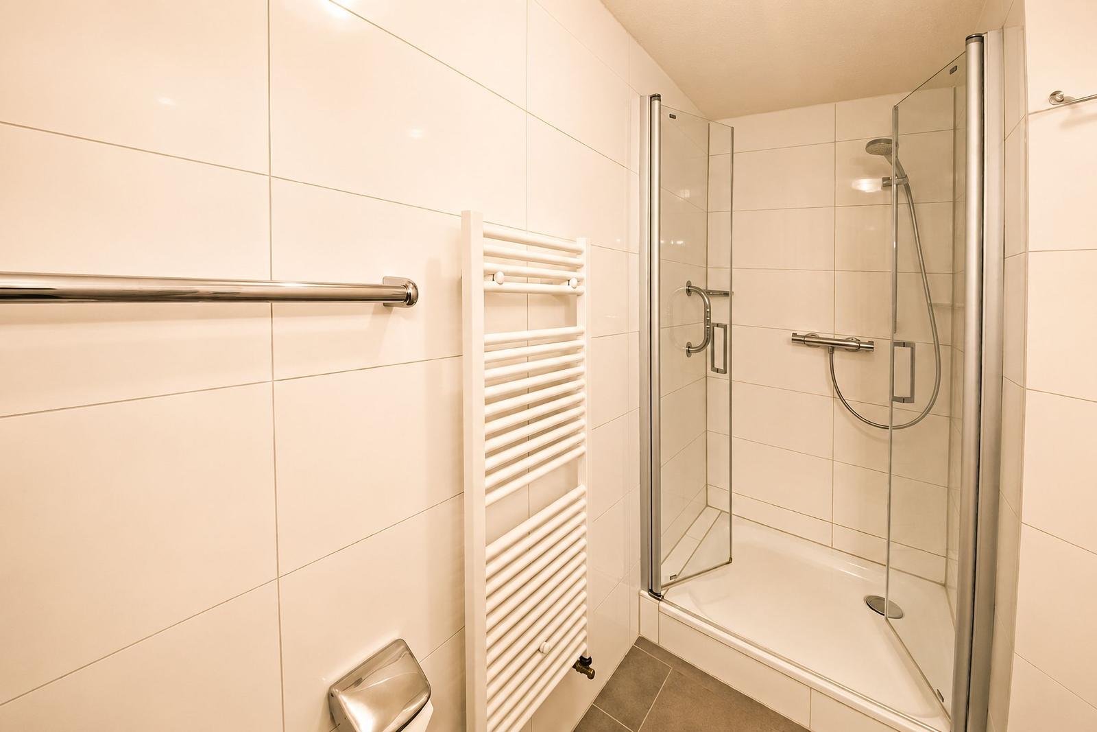 Duschkabine mit Glaswand, Heizung und Handtuchhalter an der Wand.