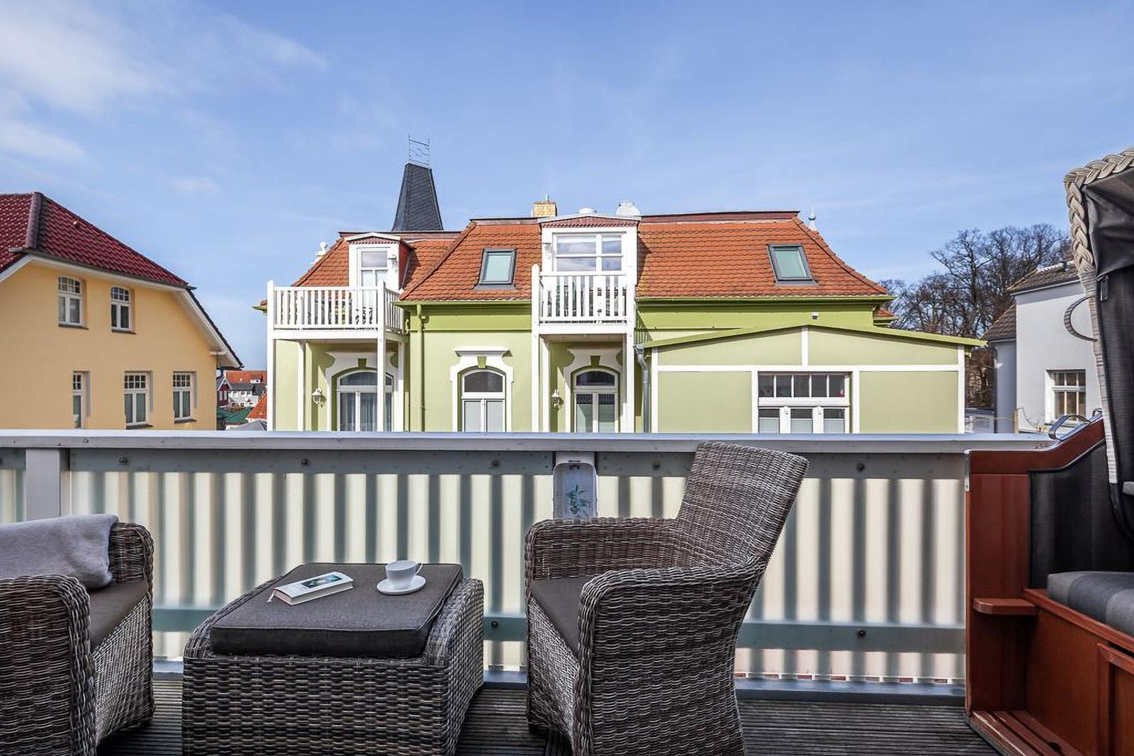 Terrasse mit Sitzgelegenheiten und Blick auf grünes Haus mit rotem Dach