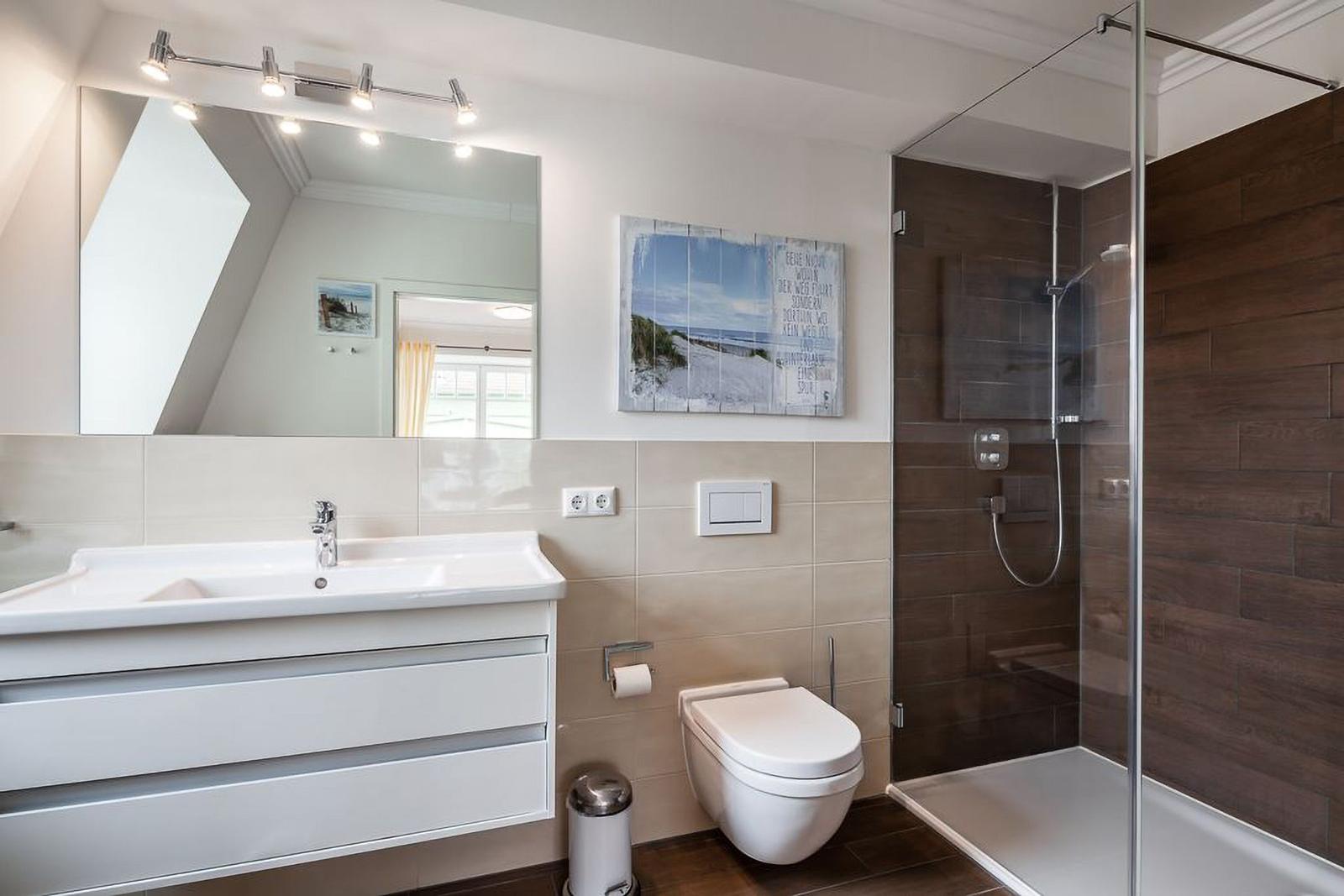 Badezimmer mit Dusche, Waschbecken und Toilette. Wandbild und Spiegel sichtbar.