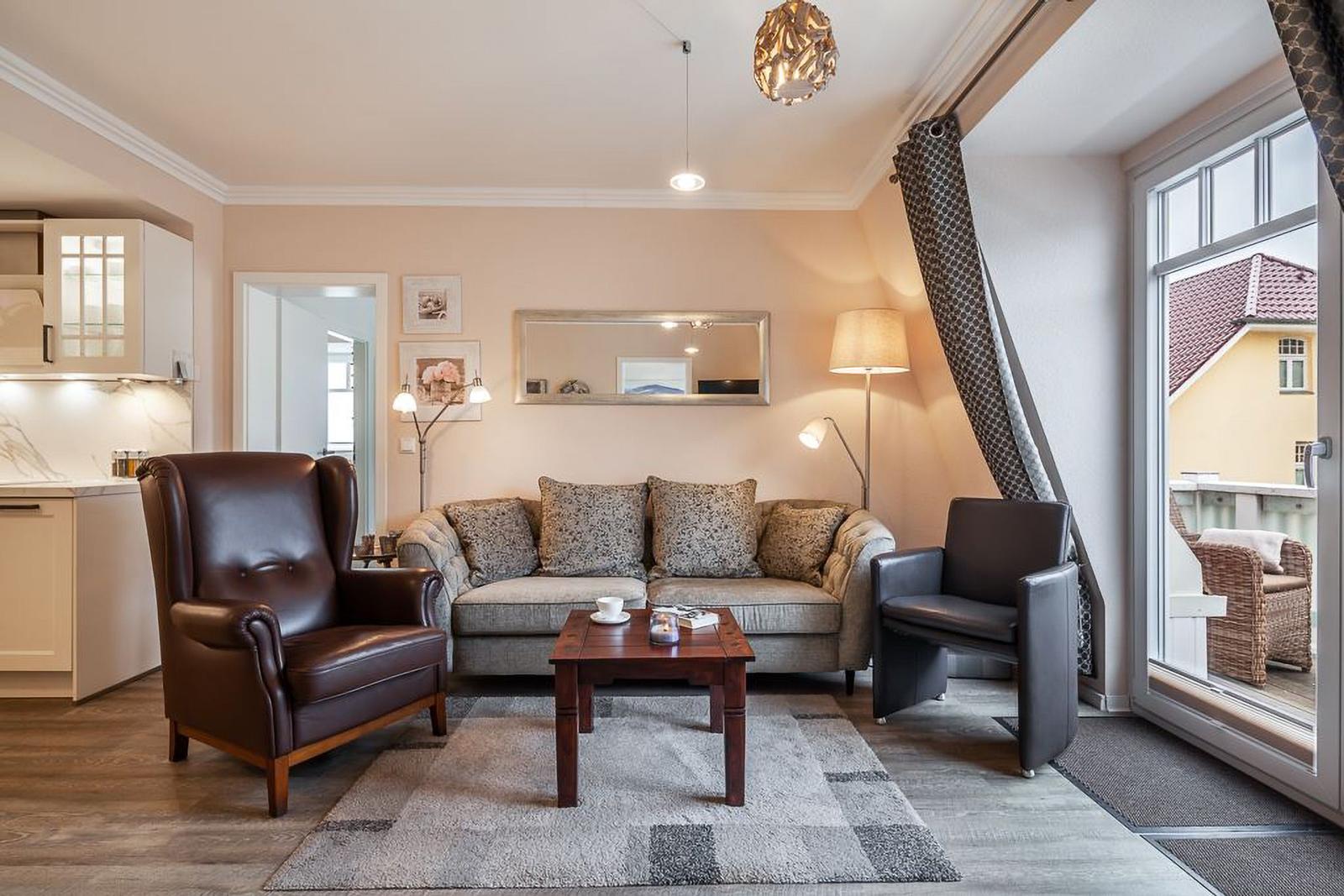 Wohnzimmer mit Sofa, zwei Sesseln und Blick auf Balkon.