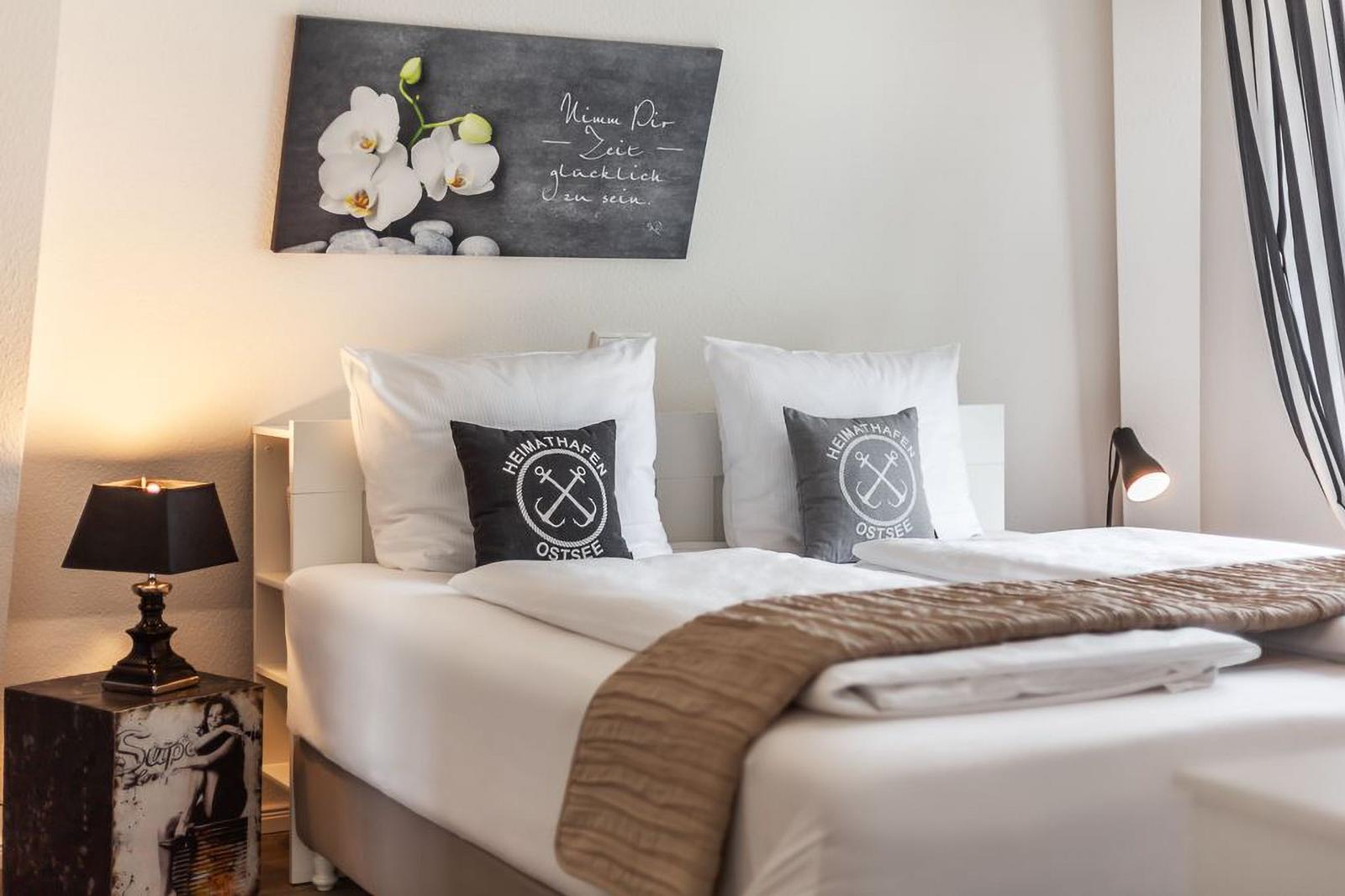 Schlafzimmer mit Bett, Kissen und Wandbild. Nachttisch mit Lampe und Vorhang.