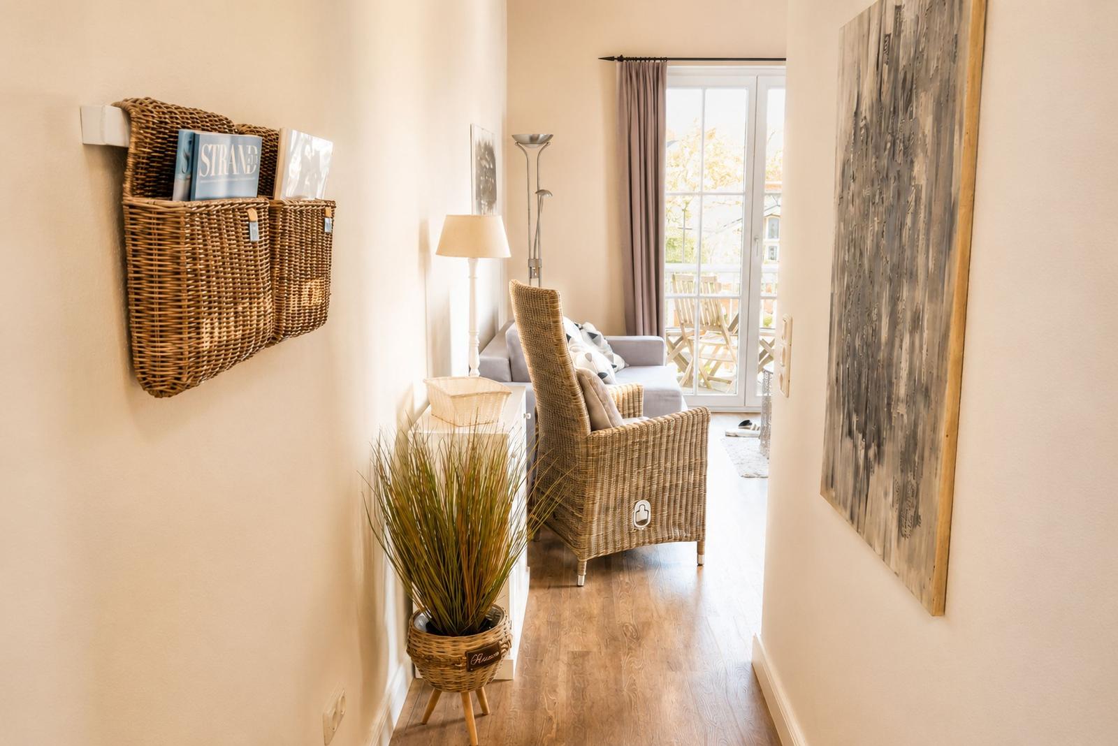 Flur mit Wickerkorb, Pflanze und Blick in Wohnzimmer mit Sitzgelegenheit.