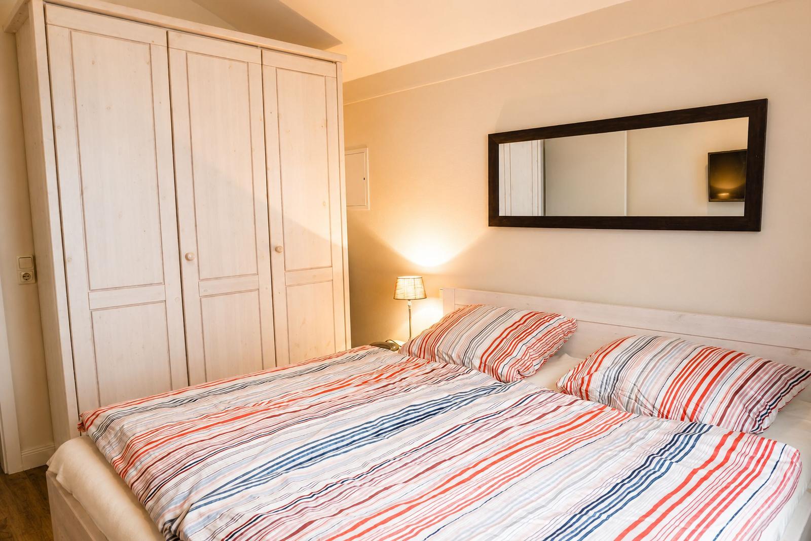Schlafzimmer mit Doppelbett, Kleiderschrank und Wandspiegel.