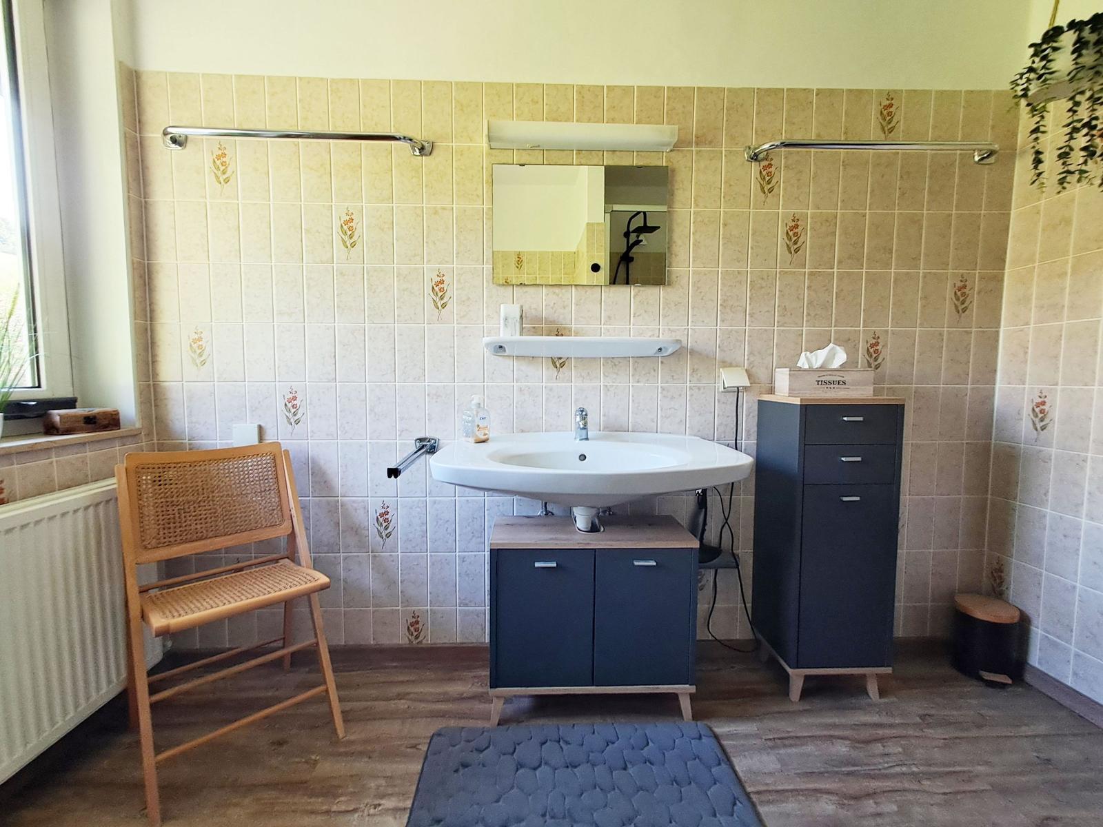 Badezimmer mit Waschbecken, Spiegel, Stuhl und Schrank.