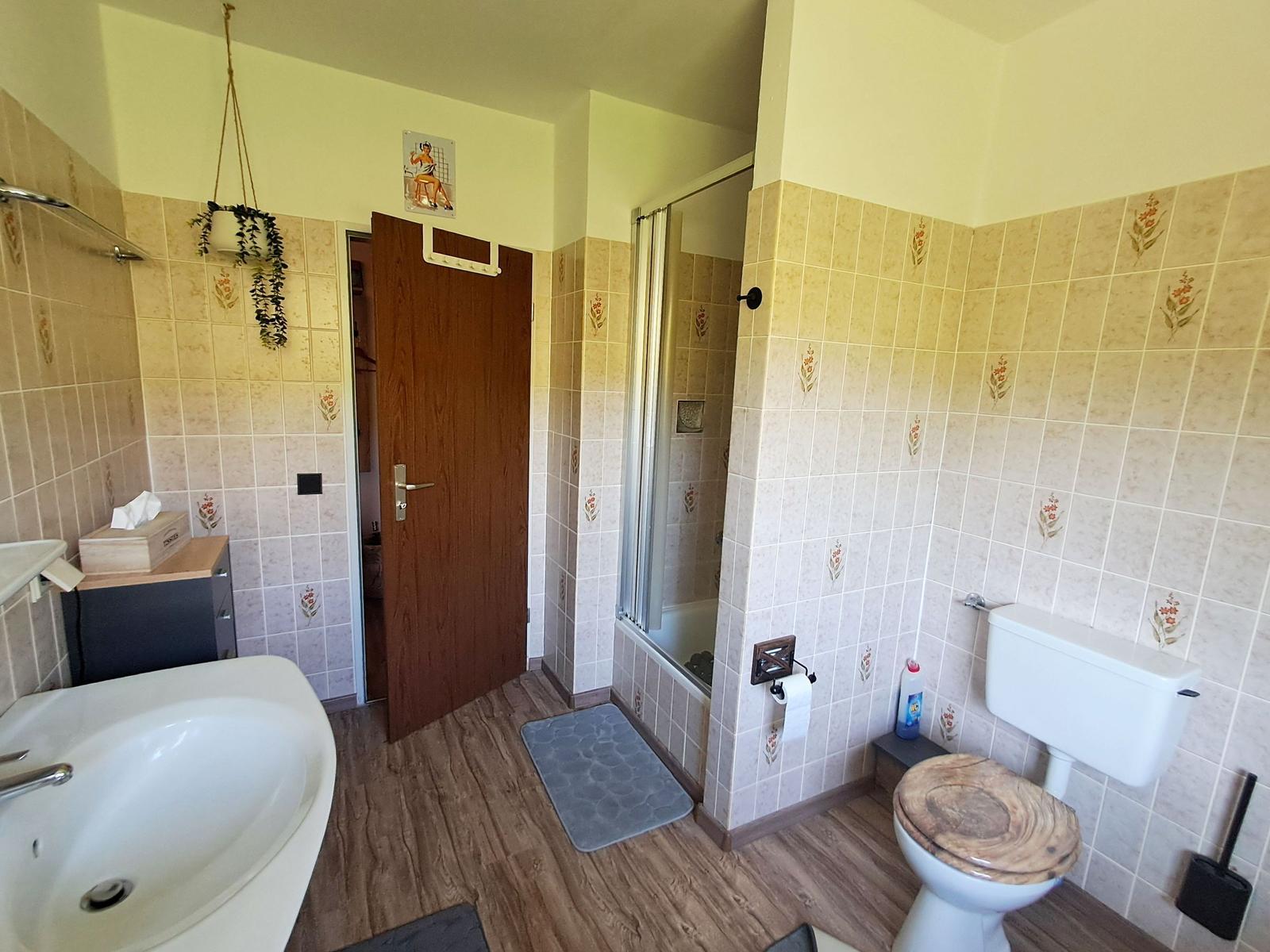 Badezimmer mit Dusche, Toilette und Waschbecken. Fliesenwand und Holzboden.