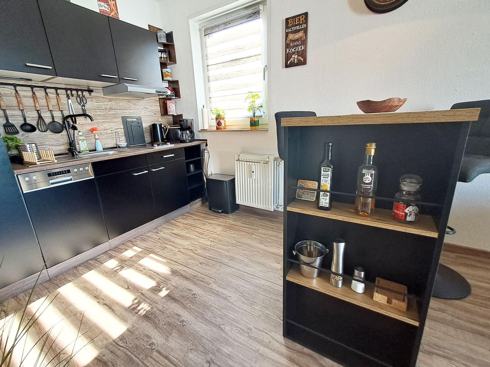 Küche mit schwarzen Schränken, Holzboden und Fenster mit Pflanzen.