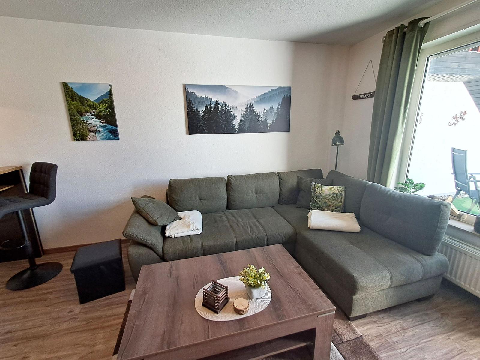 Ein Wohnzimmer mit grauem Sofa, Holztisch und Wandbildern.
